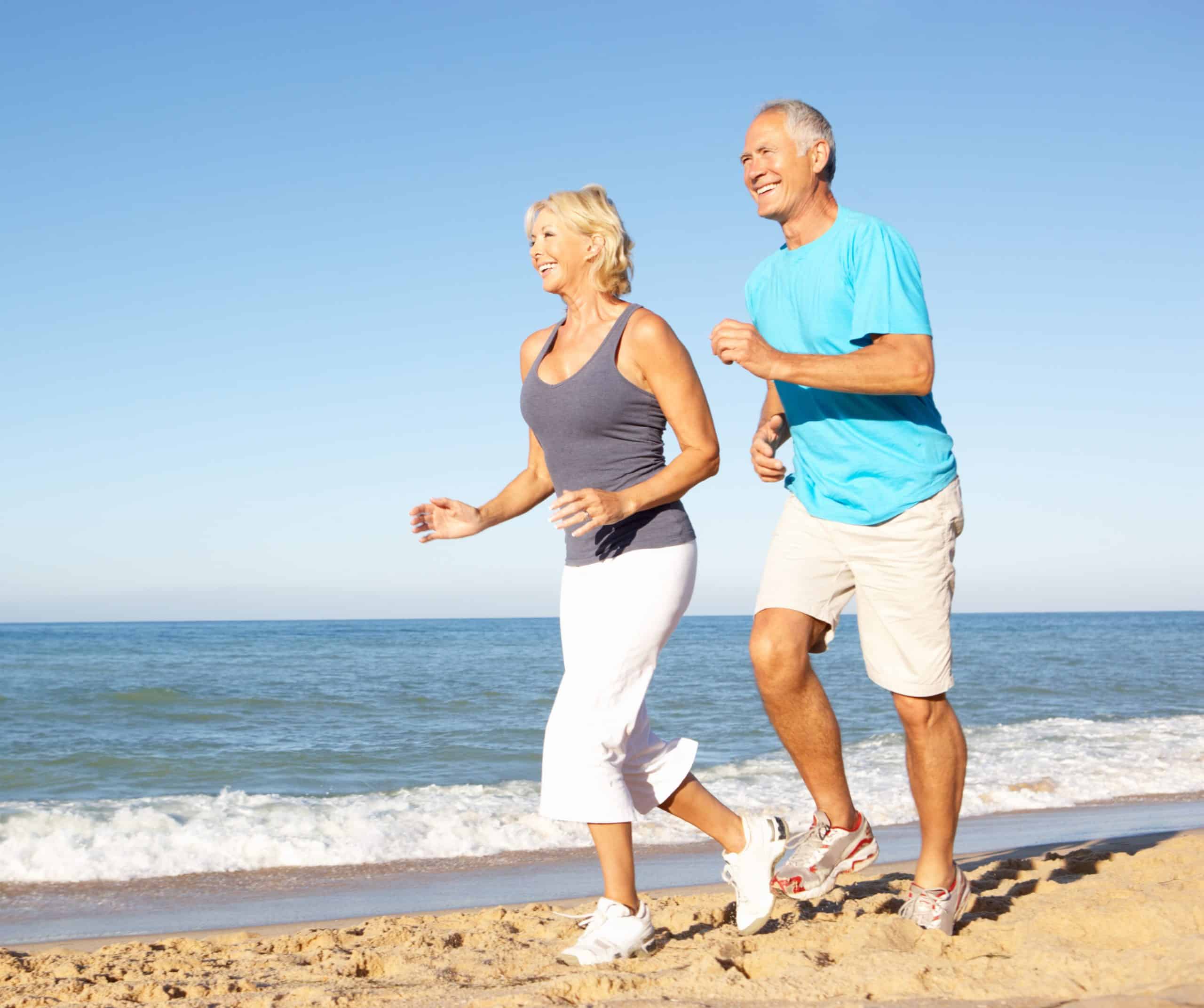 Senior Couple In Fitness Clothing Running Along Beach